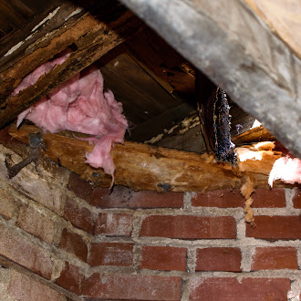 Exposed attic space showing pink insulation, wooden beams, and brick walls with visible moisture damage, one of the common signs of roof leaks in residential homes.